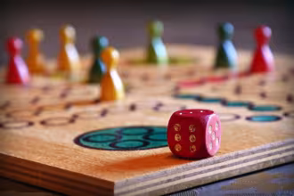 Ein Spielbrett mit Spielsteinen und einem W&uuml;rfel. Auf dem Brett sind einige Spielsteine zu sehen, die in verschiedenen Farben sind. Ein roter W&uuml;rfel liegt auf