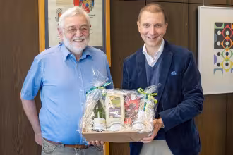 Ein ehemaliger Stadtratsmitglied h&auml;lt ein Geschenk in den H&auml;nden. Im Hintergrund ist ein Bild zu sehen.