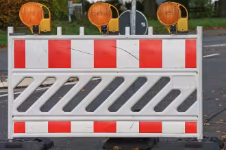 Ein Bild zeigt eine wei&szlig;e und rote Barriere mit drei orangefarbenen Leuchten auf einem Stra&szlig;enabschnitt.